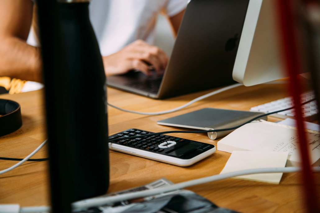 A person working at a table with laptop, card reader, phone and trackpad. Wires and papers. 