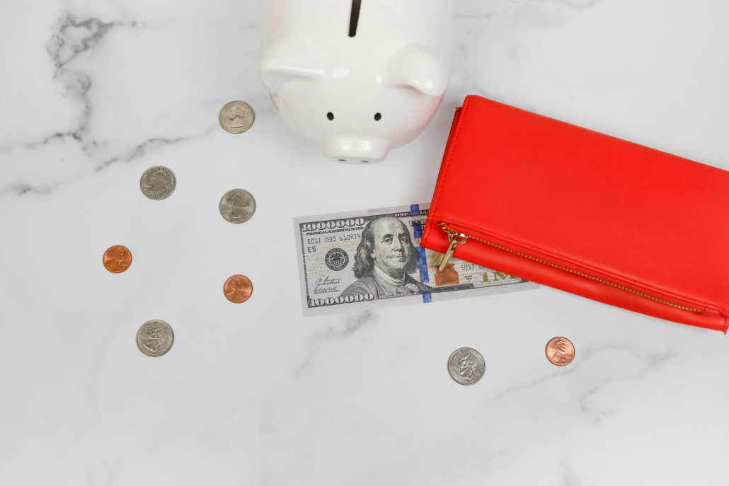 a marble surface with a pig-shaped money box, coins, $1 and a red zipped wallet